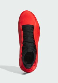 Zapatilla roja con parte superior suave, cordones negros, puntera redondeada y acentos texturizados en la suela para mayor agarre.