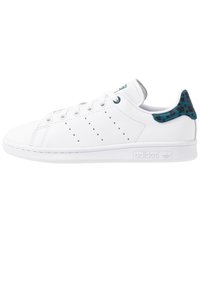 Zapatillas blancas con una parte superior de cuero suave, acentos de patrón azul en el talón, diseño clásico de cordones y detalles perforados en los lados.