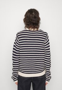 Pull en tricot rayé avec des lignes horizontales alternées bleu marine et crème, motif de points texturé, et bord-côtes à la taille et aux poignets.