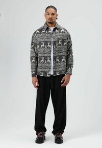 Chemise à col noire et blanche à motifs de rennes, portée sur un t-shirt blanc. Associée à un pantalon noir ample et des chaussures noires.