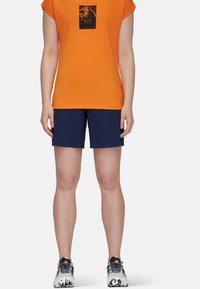 Orange kortärmad t-shirt med svart grafiskt tryck, matchad med marinblå shorts och mönstrade träningsskor.