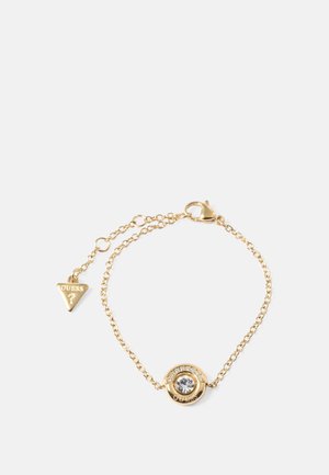 Gold metal bracelet with a circular pendant featuring a clear gemstone and surrounding rhinestones, attached to a chain with a small logo tag.