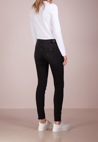 Svarta smala jeans med hög midja, bakfickor och subtil logotypdetalj. Matcher med en långärmad vit topp och vita sneakers.