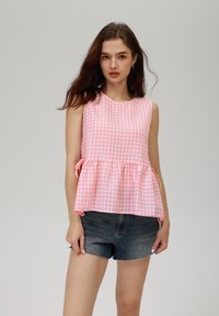 Top senza maniche a quadri rosa e bianchi con orlo a peplum e lacci laterali, abbinato a pantaloni corti di denim scuro, con scollatura rotonda.