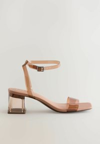 Transparent högklackad sandal med bred rem och justerbar ankelspänne. Har en fyrkantig, klar blockklack och en mjuk nude-färgad innersula.