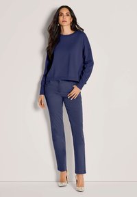 Navyblaues, kurzes Sweatshirt mit langen Ärmeln, kombiniert mit passenden, navyblauen Slim-Fit-Hosen und gemusterten, hochhackigen Schuhen in Pastellfarben.