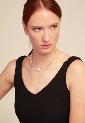 Collar de plata de múltiples hebras con un diseño texturizado y un acento central, que se lleva sobre una blusa negra con detalles de hombros fruncidos.