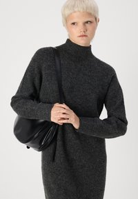 Suéter cinza de malha com um alto colarinho e corte solto, combinado com uma bolsa de couro preta. Textura suave e mangas relaxadas.