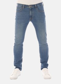 Slim-fit blauwe denim jeans met vijf zakken, riemlussen en subtiele vervaging, gecombineerd met witte sneakers op een neutrale achtergrond.
