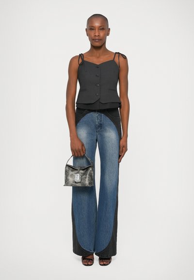 Top peplum grigio con spalline regolabili e bottoni, abbinato a jeans a zampa blu con pannello laterale nero a contrasto e borsa grigia piccola.