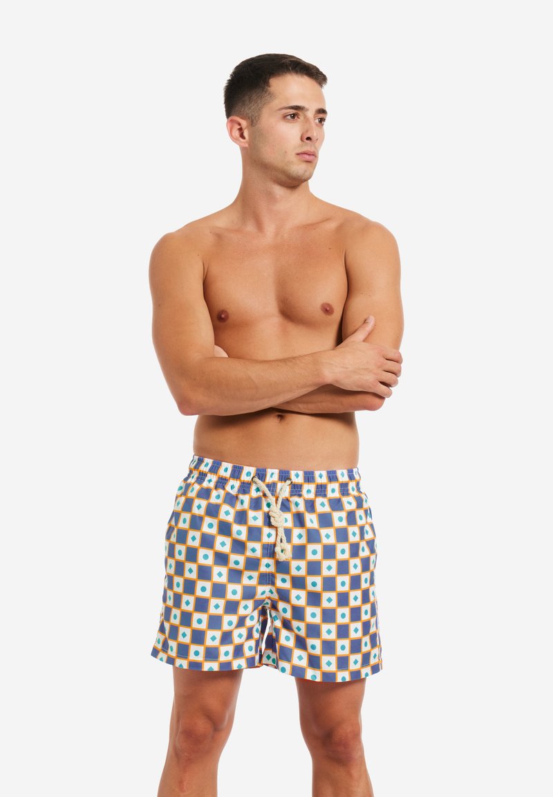 Costumi da bagno con un motivo geometrico di quadrati blu, arancioni e bianchi. Vita elasticizzata con lacci, realizzati in tessuto leggero.