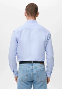 Camisa de manga larga azul claro con puños abotonados, textura suave y cuello estructurado, combinada con jeans de mezclilla azul claro y un cinturón negro.