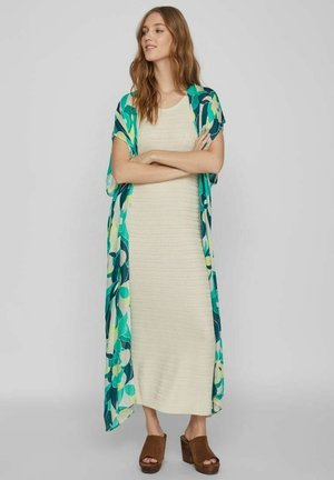 Maxikleid aus strukturiertem cremefarbenem Stoff, darüber eine kimonoartige Jacke mit tealfarbenem und grünem Blumenmuster. Braune Plateausandalen runden das Outfit ab.