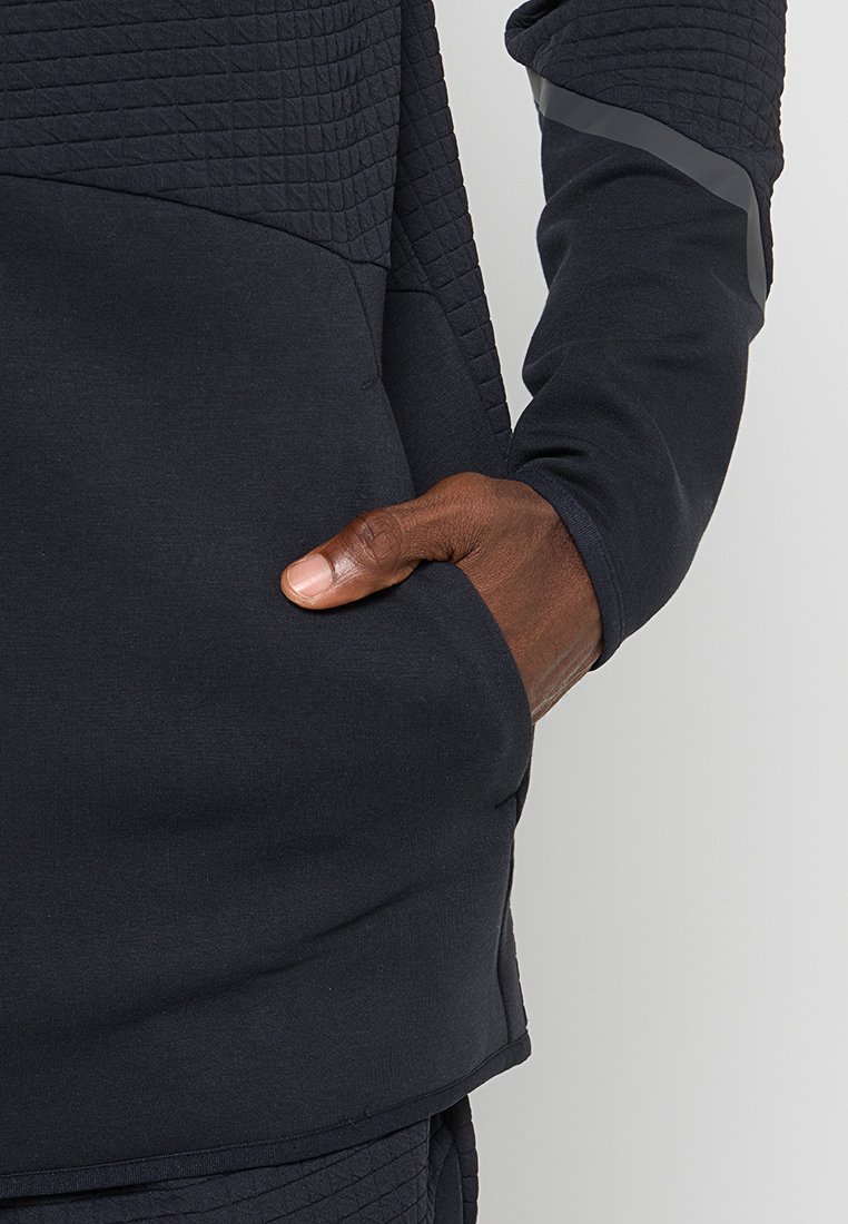 Maglione navy con pannelli trapuntati testurizzati, maniche lunghe e tasca frontale. Presenta accenti grigi sulle maniche. Tessuto morbido, vestibilità rilassata.