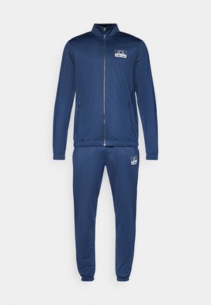 Námořnický modrý teplákový komplet vyrobený z hladké látky, zahrnující bundu na zip se stojáčkem a kalhoty s elastickým pasem. Logo na obou kouscích.