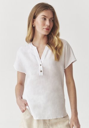 Bílý lněný top s krátkým, mírně rozšířeným rukávem, polo-cedníkem a volnějším střihem. Hladká textura s minimálními designovými detaily.