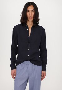 Marineblaues Leinenhemd mit Knöpfen und lockerer Passform, silberne Knöpfe, kombiniert mit hellblauen elastischen Hosen mit Gummizug, minimalistisches Design.