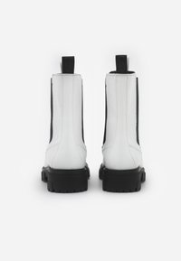 Botas de tobillo de cuero blanco con paneles laterales elásticos negros y bucles de agarre, cuentan con una suela de goma negra gruesa y detalles de costura.