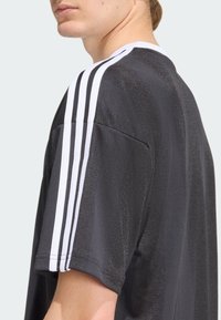 Melna sporta krekls ar baltām svītrām uz pleciem, īsām piedurknēm, struktūrētu audumu un apļa kakla izgriezumu.