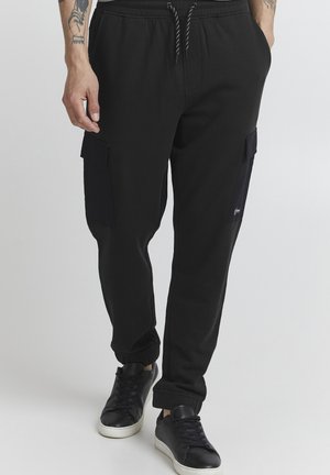 Black sweatpants with a drawstring waist, featuring side cargo pockets in a contrasting dark material and ribbed ankle cuffs.