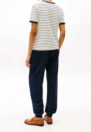 Koszulka z bawełny w paski z niebieskimi akcentami, w zestawie z granatowymi dresami i brązowymi mokasynami. Posiada luźny krój i miękkie tekstury.