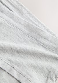 Gros plan sur un tissu gris clair avec des coutures visibles et une texture subtile, mettant en valeur les détails des coutures et les plis doux du matériau.