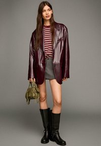 Blazer oversize in pelle bordeaux, top a righe bordeaux e bianche, mini gonna grigia, stivali neri sopra il ginocchio, borsa verde oliva con frange.