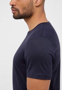 T-shirt in cotone blu navy con collo a giro, maniche corte e una texture liscia, che mostra una vista laterale della vestibilità e della forma.