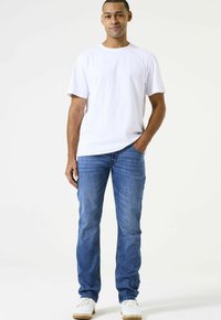 Camiseta de algodón blanca combinada con vaqueros de mezclilla azul y zapatillas blancas. La camiseta tiene un cuello redondo, y los vaqueros presentan un ligero desgaste con un corte recto.