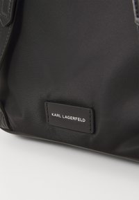 Black fabric bag with a smooth texture. Features a rectangular brand patch with white text reading "KARL LAGERFELD." Minimalistic design.