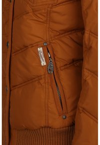 Orange quiltet jakke lomme med synlig lynlås, mærket metaltræk, stofmærke, trykknapper og ribbet talje detalje.