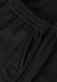 Zwarte broek met een elastische tailleband, voorzien van zijzakken en een zachte, gestructureerde stof. Het ontwerp is casual en veelzijdig.