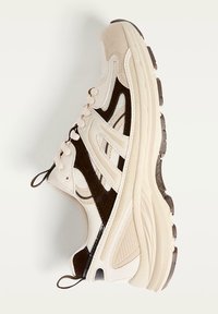 Chaussure présentant un coloris beige et marron, en matériau mesh, avec une semelle rembourrée et un design lacé, ainsi qu'une semelle extérieure en caoutchouc texturé.