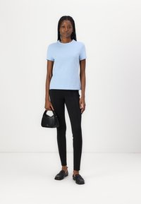 T-shirt en coton bleu clair, à manches courtes, associé à un pantalon noir ajusté et un petit sac noir. Texture lisse avec un minimum de détails.