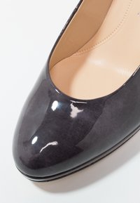 Chaussure pour femme en cuir verni noir brillant, à bout arrondi et doublure intérieure beige rembourrée.