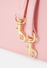Różowa torba z ekologicznej skóry ze złotymi okuciami i dwoma zatrzaskami. Charakteryzuje się gładką fakturą i widocznym przeszyciem na krawędziach.