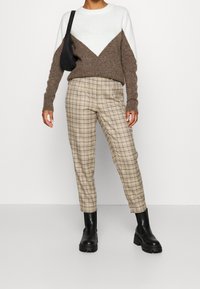 Brun och vit färgblockad tröja med V-formad design, som matchas med rutiga beige byxor och svarta kängor med tjocka sulor. Svart axelväska.