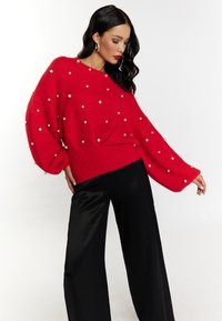 Pulover roșu supradimensionat cu embellismente din perlă, textură tricotată și mâneci largi, asortat cu pantaloni negri cu picioare largi.