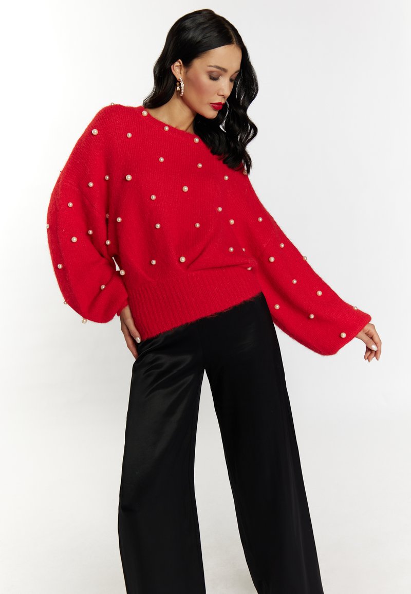Pulover roșu supradimensionat cu embellismente din perlă, textură tricotată și mâneci largi, asortat cu pantaloni negri cu picioare largi.