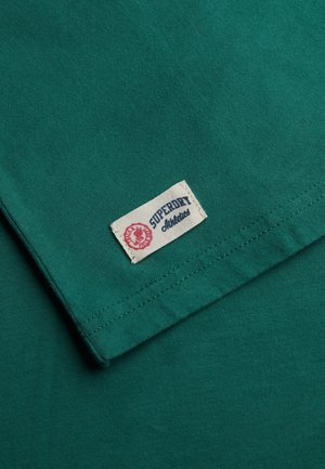 Groen katoenen T-shirt met een Superdry-label. De stof is glad met een lichte glans en toont nette stiksels langs de zoom.