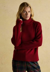 Punane kõrge kaelusega sviiter ribatekstuuriga ja pikkade varrukatega, koos plüüšträäkide püksidega. Kanga välimus on pehme ja paks.