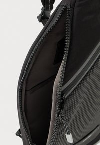 Mochila negra de tela texturizada, con cierre de cremallera suave y forro interior gris con patrón de cuadrícula. Bolsillo interior visible.