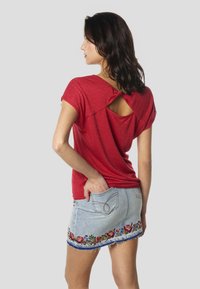 Červený top s krátkym rukávom a výrezom na chrbte, doplnený vybledlou rifľovou sukňou s kvetinovou výšivkou na leme a ošúchanými okrajmi.