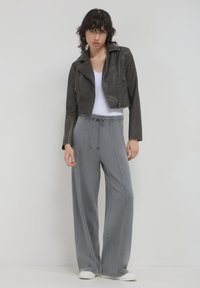 Veste grise en cuir coupée avec poches zippées, associée à un pantalon gris ample avec taille élastique et cordon de serrage, porté avec des baskets blanches.
