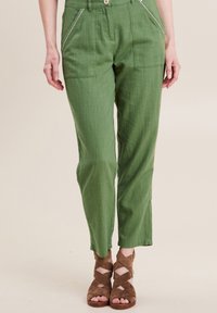Groene linnen broek met voorste patchzakken, contrasterende stiksels en een rechte pijp. Draagt het met bruine gewikkelde sandalen.