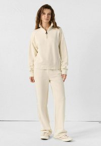 Crème-kleurige, zachte fleece pullover met een ritssluiting bij de kraag en bijpassende fleece broek. Eenvoudig ontwerp met een relaxte fit en minimale accenten.