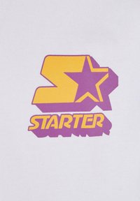 Hvit bomull t-skjorte med grafikk i lilla og gul, som viser et stilisert "S" og en stjerne ved siden av ordet "STARTER."