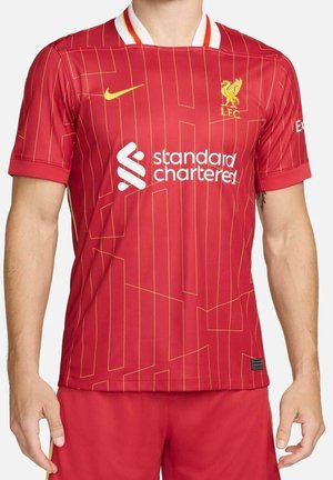 Maillot de football rouge du Liverpool FC avec des fines rayures dorées, logo Nike jaune et logo sponsor Standard Chartered blanc sur le torse d'une personne.