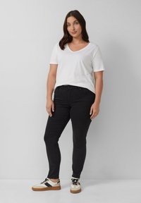 Biely tričko s v-výstrihom, priliehajúce čierne džínsy a béžové tenisky s čiernymi pruhmi a hnedými podrážkami. Hladká tkanina, neformálny dizajn.