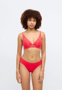 Soutien-gorge en dentelle rouge avec un motif floral et des bretelles ajustables, associé à des culottes en dentelle rouge assorties. Texture lisse, design sans couture.